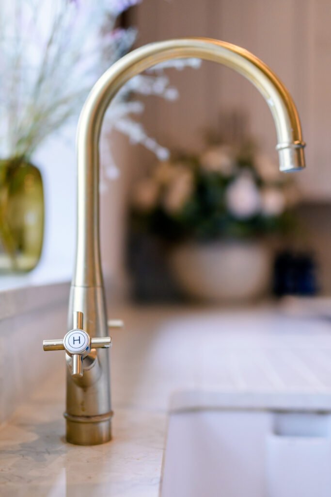 Close-up of gold kitchen tap with blurred floral background – Residential project “Cloyne Farmhouse Part One”, designed by AK Interior, Cork, Ireland.