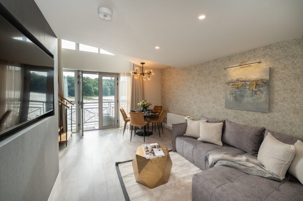 Living room with a grey sofa, gold coffee table and large windows overlooking the terrace. West Cork Waterfront project by AK Interior, Cork, Ireland.
