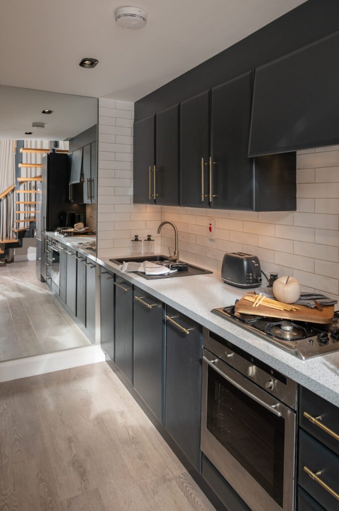 Kitchen with black cabinets, light countertop and staircase in the background. West Cork Waterfront project by AK Interior, Cork, Ireland.