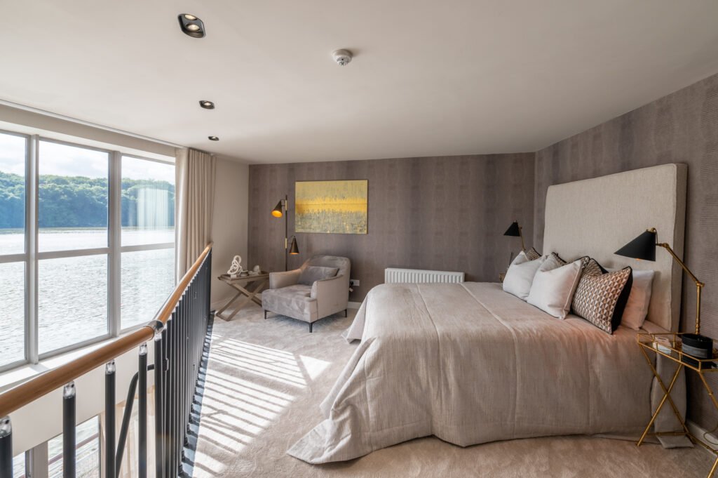 Bedroom with a large window and double bed with grey headboard. West Cork Waterfront project by AK Interior, Cork, Ireland.