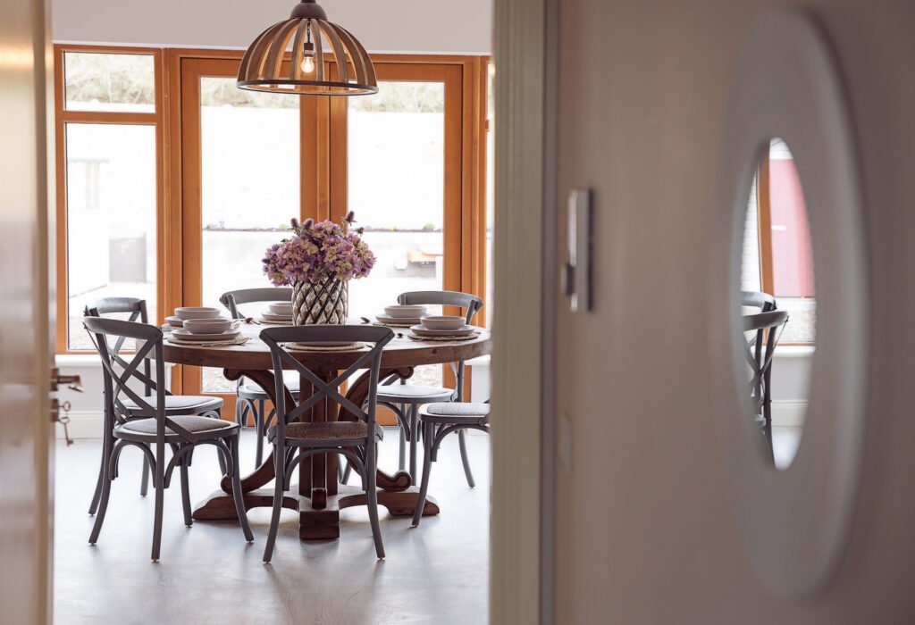 Round dining table with dark wooden chairs and a flower centerpiece in a bright room – Innishannon Showhouse by AK Interior, Cork, Ireland