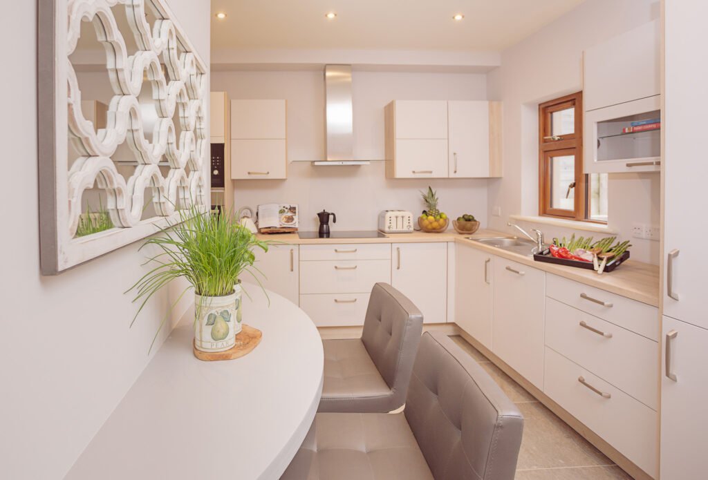 Bright modern kitchen with white cabinetry, curved breakfast bar and decorative mirror – Innishannon Showhouse by AK Interior, Cork Ireland.