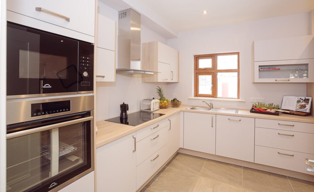 Contemporary white kitchen with built-in oven, wood countertops and sleek storage – Innishannon Showhouse by AK Interior, Cork Ireland.