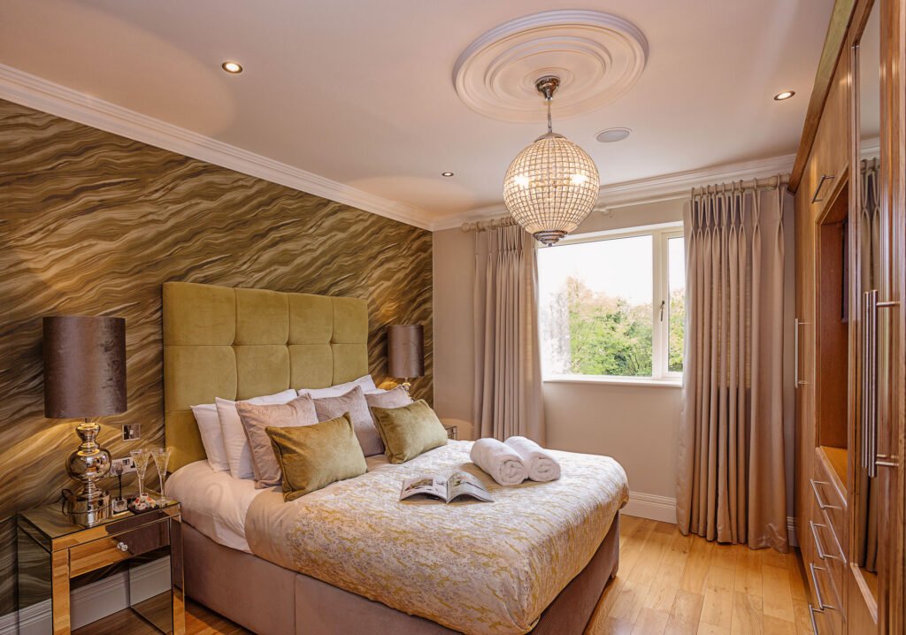 Side view of patterned-wall bedroom with mustard headboard and window bringing in daylight. Rockport Residential project, AK Interior, Cork.