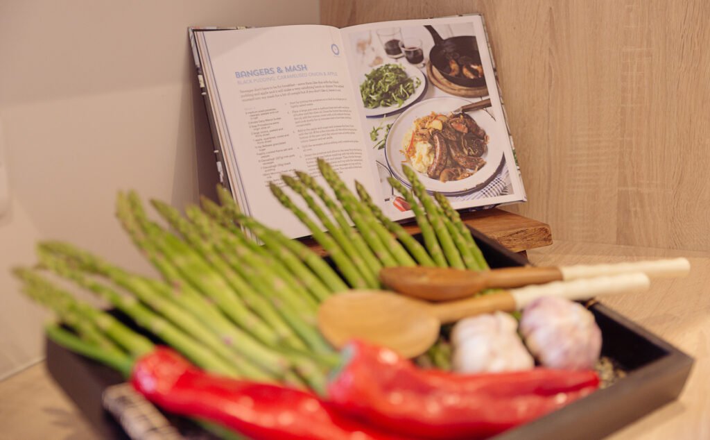 Fresh asparagus, peppers and garlic displayed beside an open cookbook on a kitchen counter – Innishannon Showhouse by AK Interior, Cork Ireland.