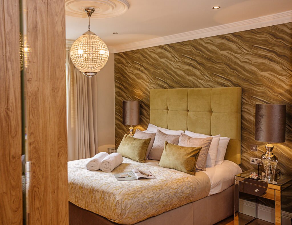 Guest bedroom with mustard headboard, patterned feature wall and neatly folded towels on bed. Rockport Residential project, AK Interior, Cork.