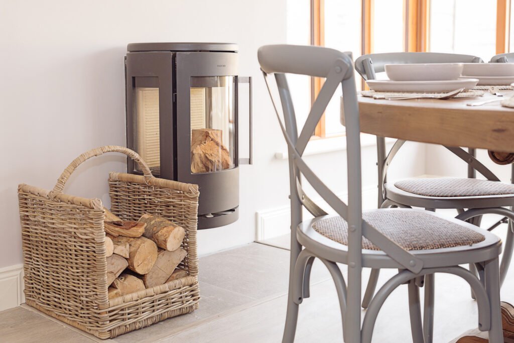 Wood-burning stove with basket of firewood beside dining table – Innishannon Showhouse by AK Interior, Cork Ireland.