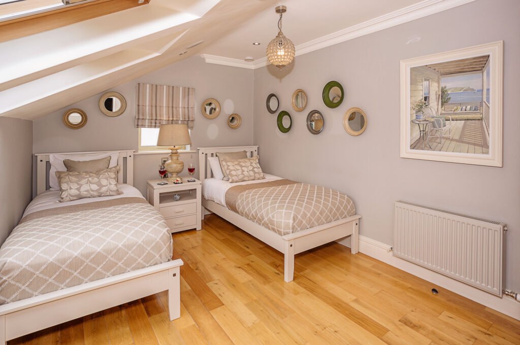 Attic twin bedroom with sloped ceiling, decorative plates and coastal artwork. Rockport Residential project, AK Interior, Cork.