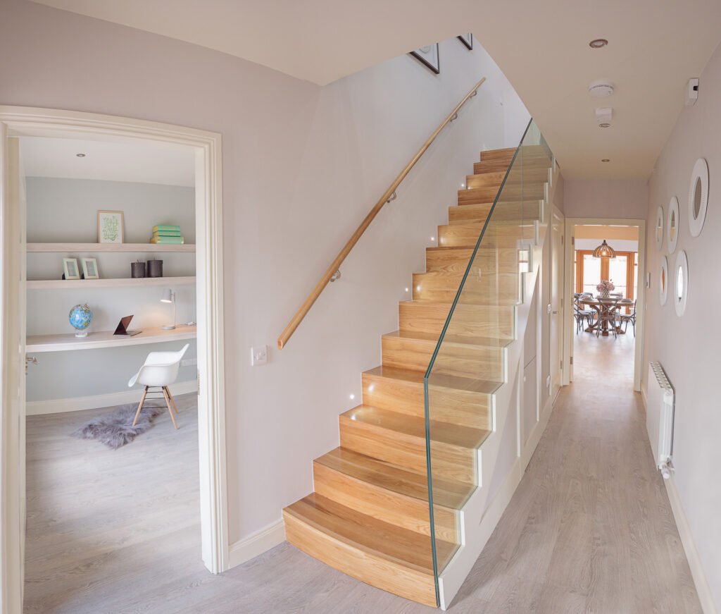 Bright hallway with glass-panel staircase and view into home office area – Innishannon Showhouse by AK Interior, Cork Ireland.