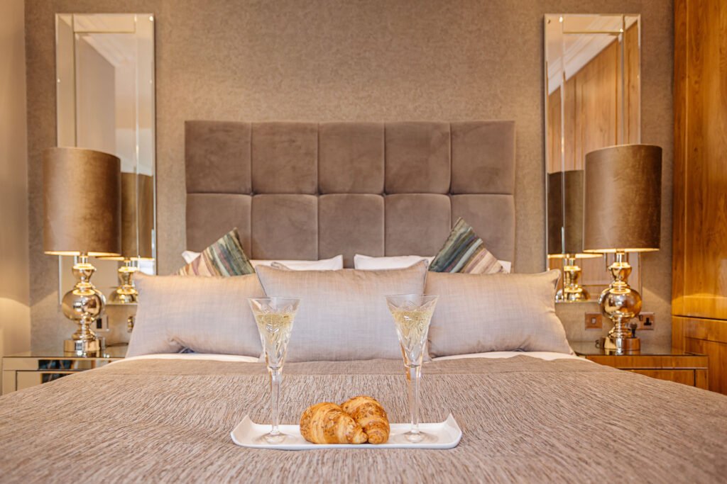 Cosy bedroom with neutral bedding, mirrored bedside tables and breakfast tray with croissants. Rockport Residential project, AK Interior, Cork.