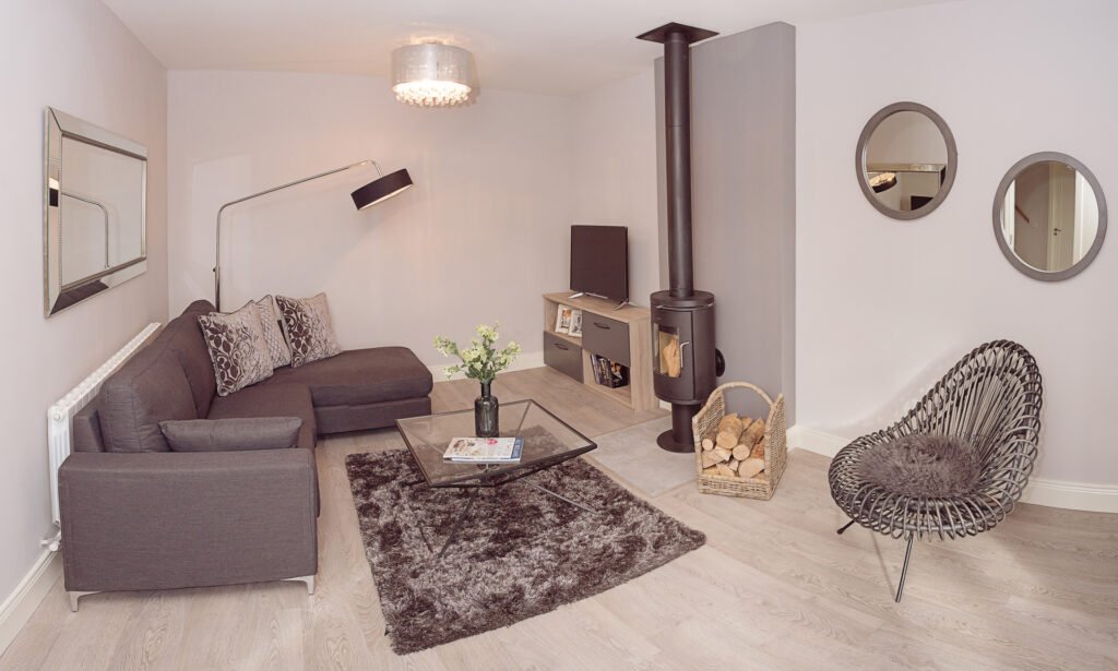 Cozy living room with grey sofa, wood-burning stove and modern circular mirrors – Innishannon Showhouse by AK Interior, Cork Ireland.
