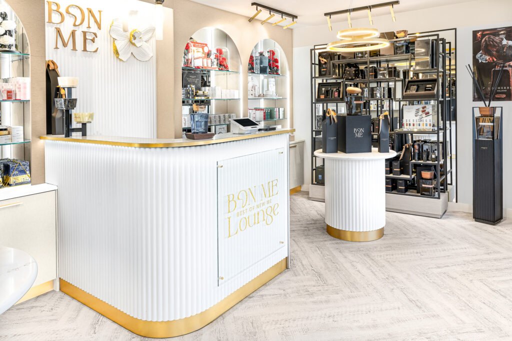 Reception area with BON ME Lounge branding, central display table and gold-accented shelving – Bon Me project, designed by AK Interior Cork.