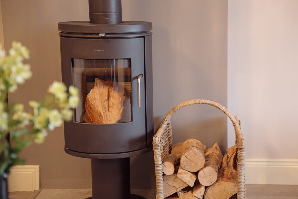 Modern wood-burning stove with wicker firewood basket in cozy living room – Innishannon Showhouse by AK Interior, Cork Ireland.