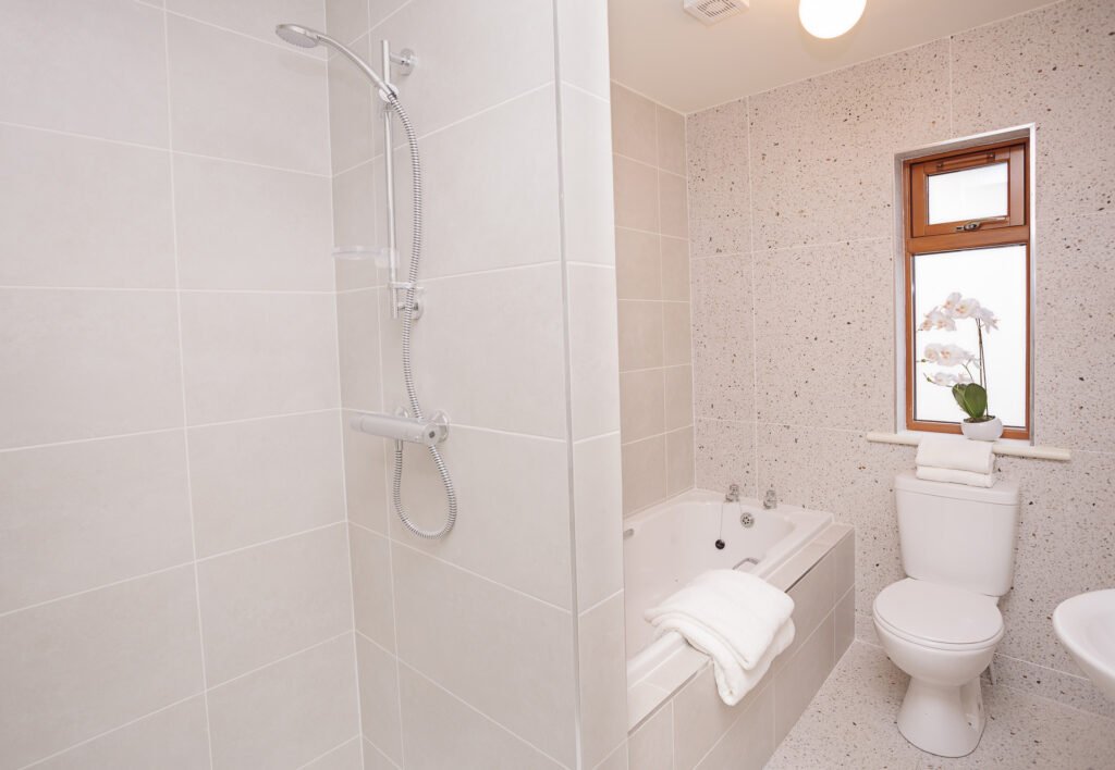 Modern bathroom with tiled shower, bathtub and natural light from window – Innishannon Showhouse by AK Interior, Cork Ireland.