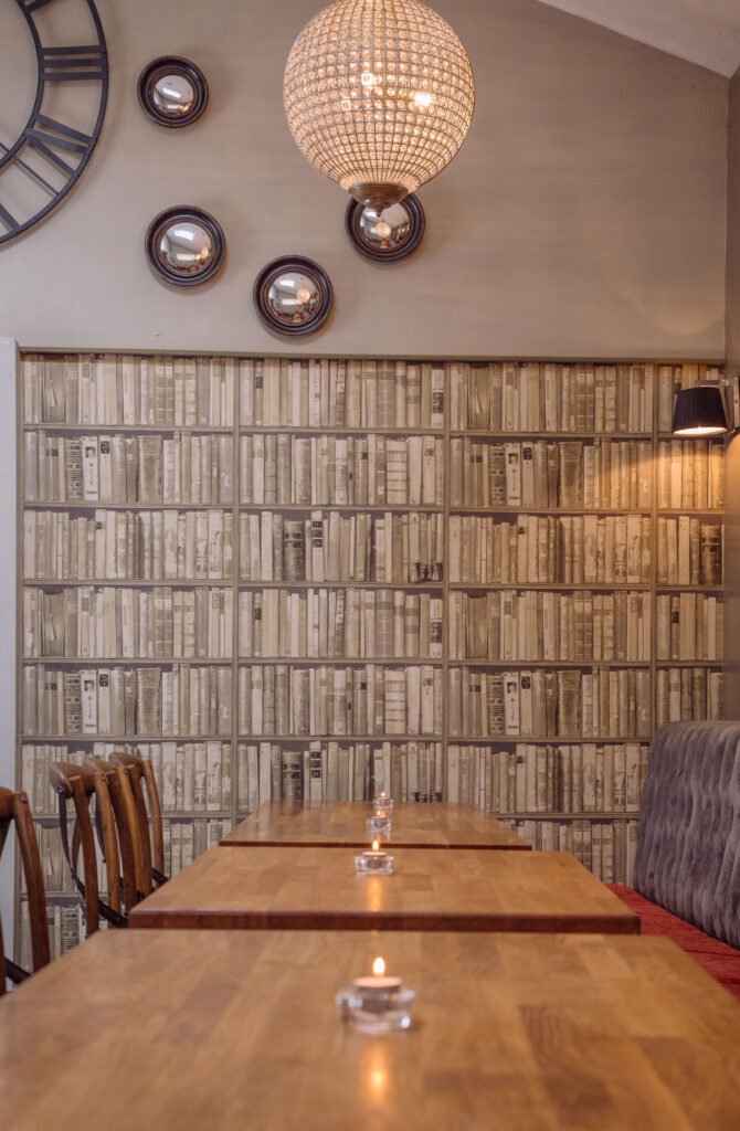 Dining table set against full-height book wallpaper feature wall. Briar Rose Commercial project, AK Interior, Cork.