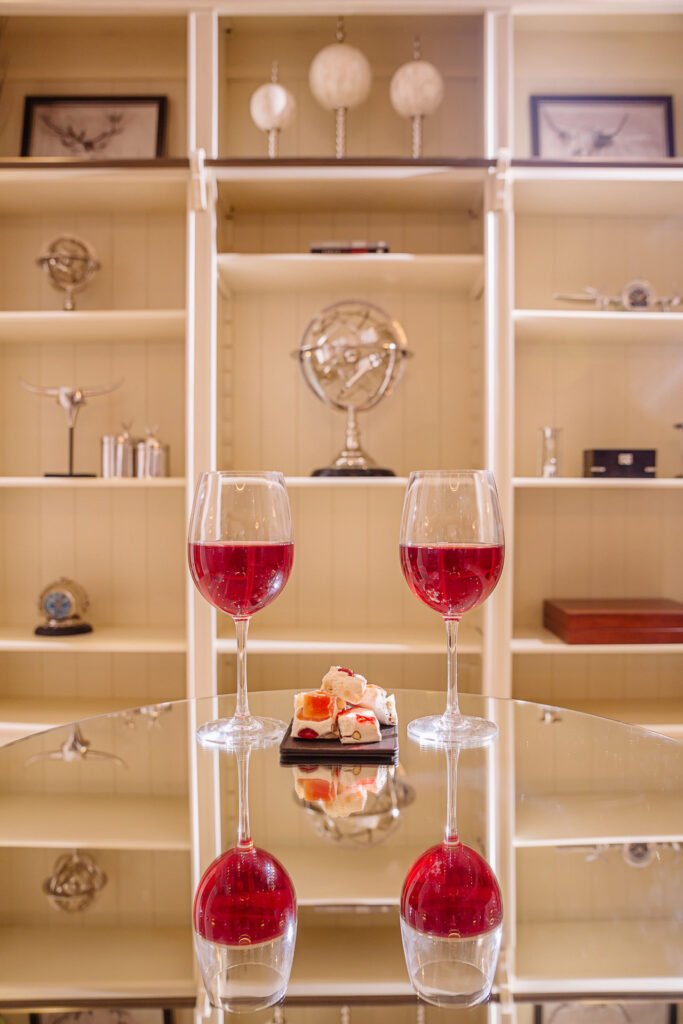 Two red wine glasses and dessert reflected in a mirrored table in front of display shelves. Rockport Residential project, AK interior.