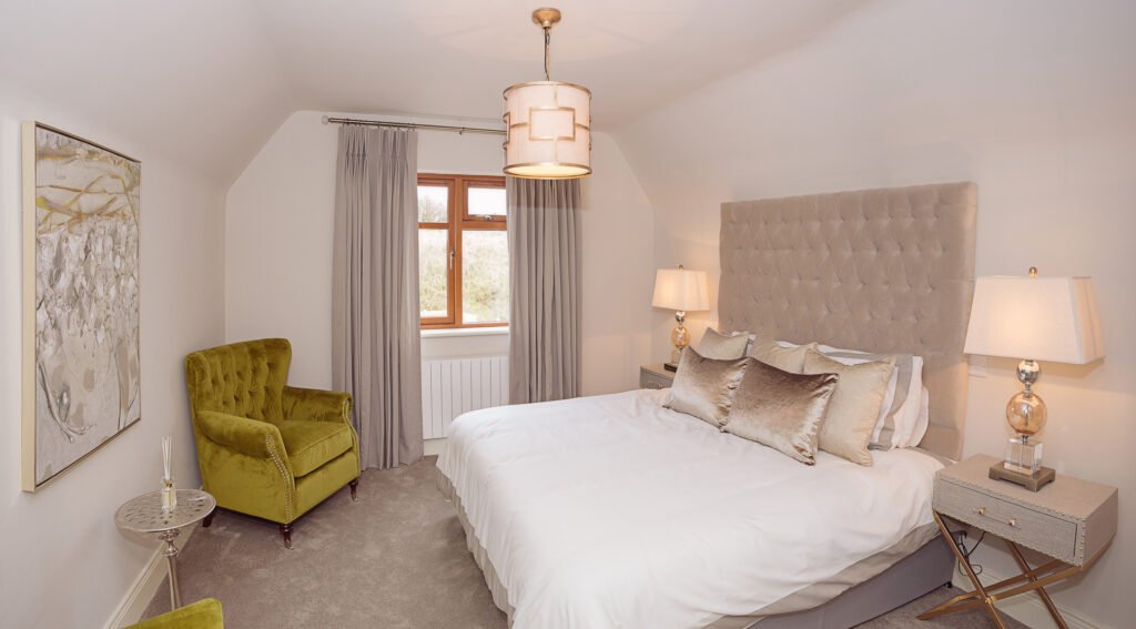 Bedroom with tufted grey headboard, white bedding and green accent cushions – Innishannon Showhouse by AK Interior, Cork Ireland.