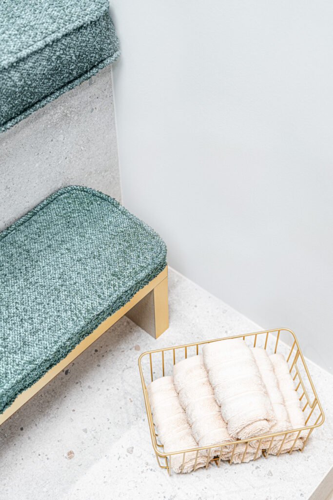 Green upholstered bench with a gold basket of rolled towels on concrete steps – Bon Me project, designed by AK Interior Cork.