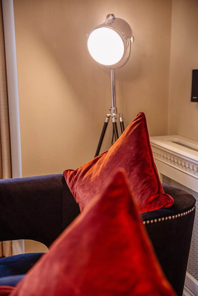 Detail of tripod floor lamp behind black armchair with bold orange velvet cushions. Rockport Residential project, AK interior.