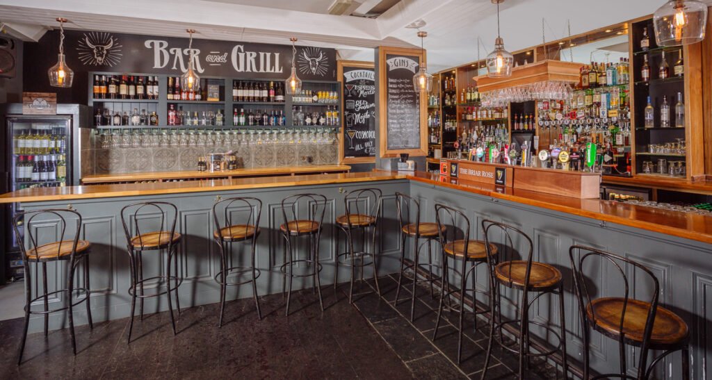 Bar counter with rows of high stools and illuminated bottle display behind. Briar Rose Commercial project, AK Interior, Cork.