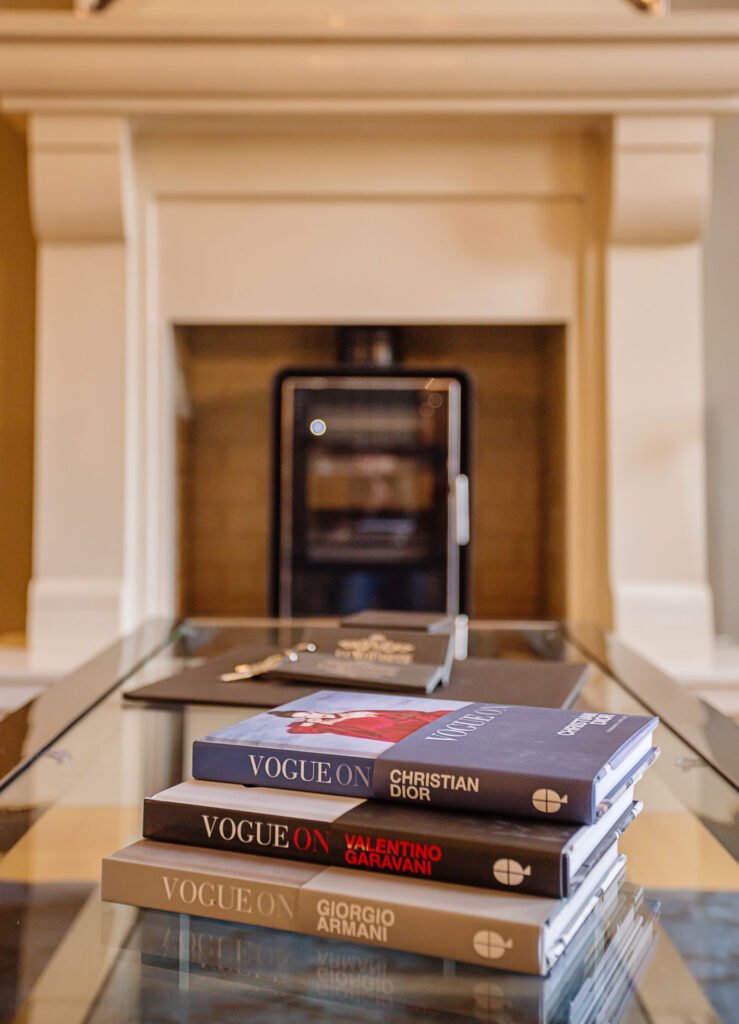 Glass coffee table styled with fashion books in front of stone fireplace surround. Rockport Residential project, AK interior.