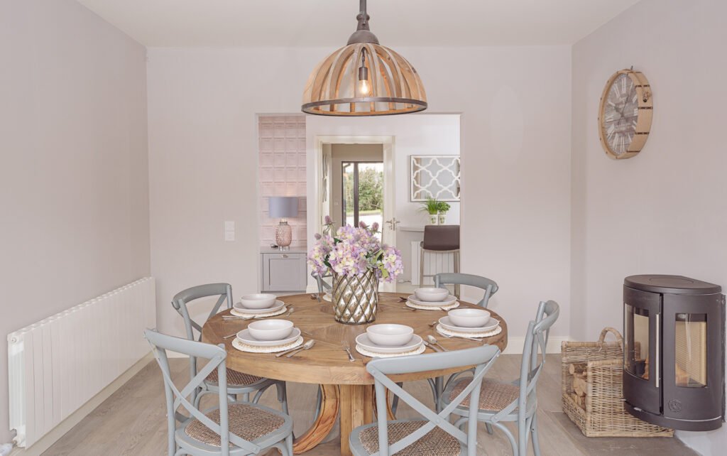 Dining area with round wooden table, six grey chairs, pendant light and wood-burning stove – Innishannon Showhouse by AK Interior, Cork Ireland.