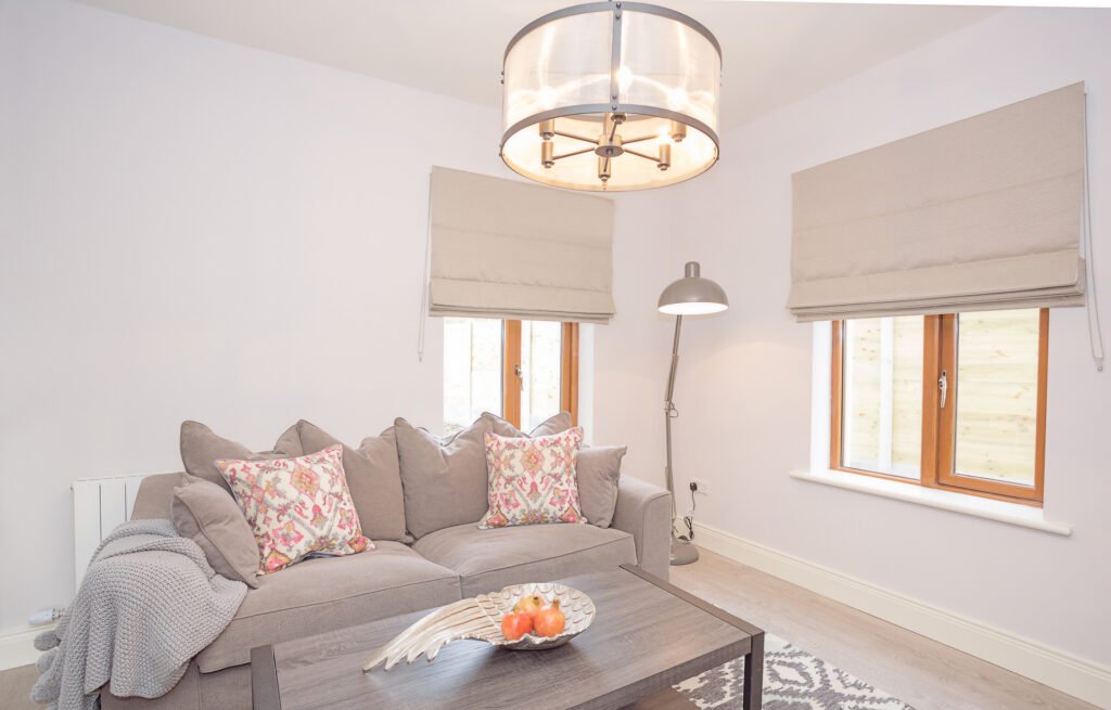 Bright living room with grey sofa, patterned cushions and large window blinds – Innishannon Showhouse by AK Interior, Cork Ireland.
