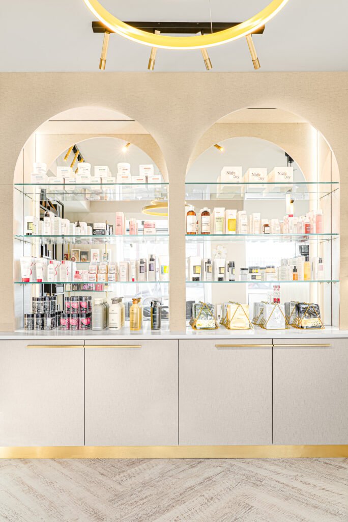 Arched glass display shelves filled with beauty products and gold accent details – Bon Me project, designed by AK Interior Cork.