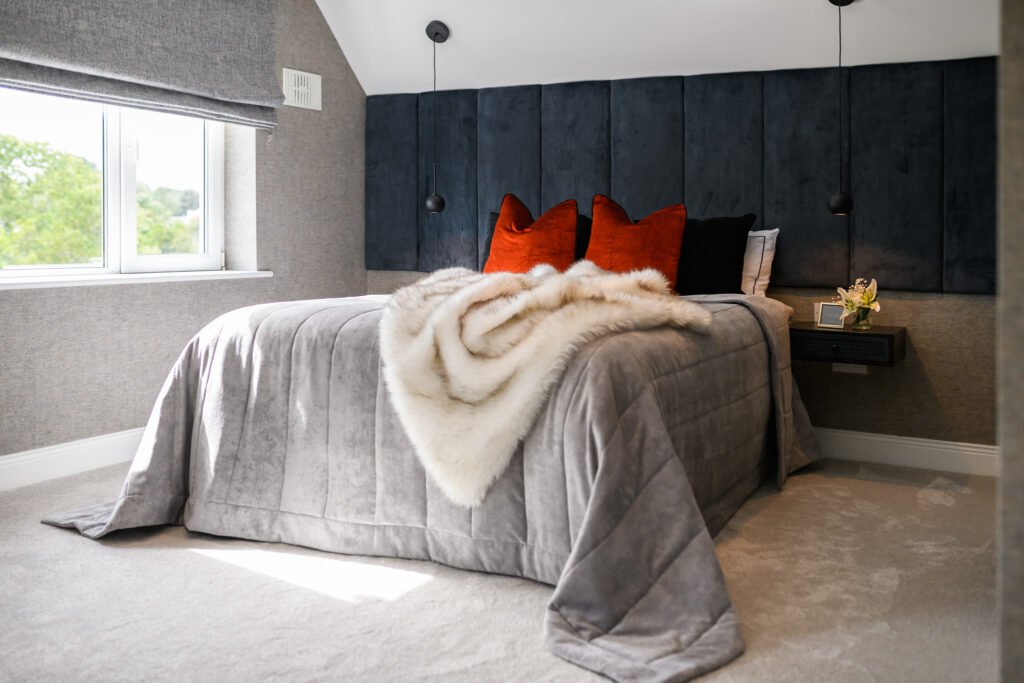 Bright bedroom with large window, grey roman blind and cosy bed featuring rust cushions and faux fur throw, AK Interior Design, Cork, Ireland