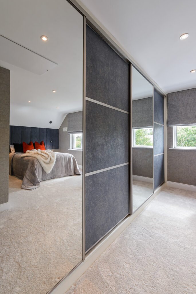 Built-in mirrored sliding wardrobes reflecting navy headboard and bed in contemporary bedroom, AK Interior Design, Cork, Ireland