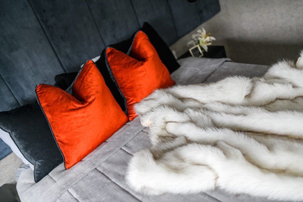 Orange velvet cushions styled on grey bed with luxurious faux fur throw in navy headboard bedroom, AK Interior Design, Cork, Ireland