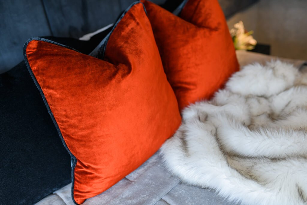 Burnt orange cushions and white faux fur throw styled on a soft grey bedspread in a modern bedroom, AK Interior Design, Cork, Ireland