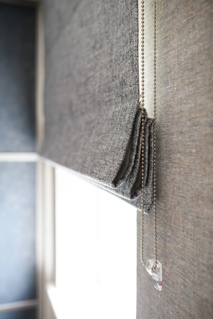 Close-up of grey textured roman blind with chain detail beside bedroom window, AK Interior Design, Cork, Ireland