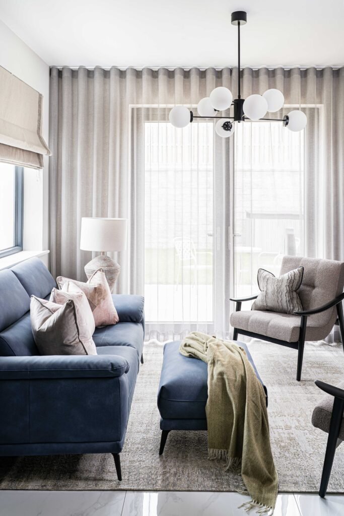 Bright living room with blue sofa, layered curtains and modern chandelier – Residential project “The Steeples Part One”, designed by AK Interior, Cork, Ireland.