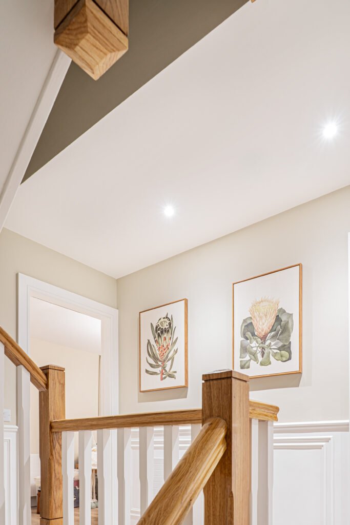 Open staircase with natural wood banister and gallery wall artwork — The Steeples Part One by AK Interior