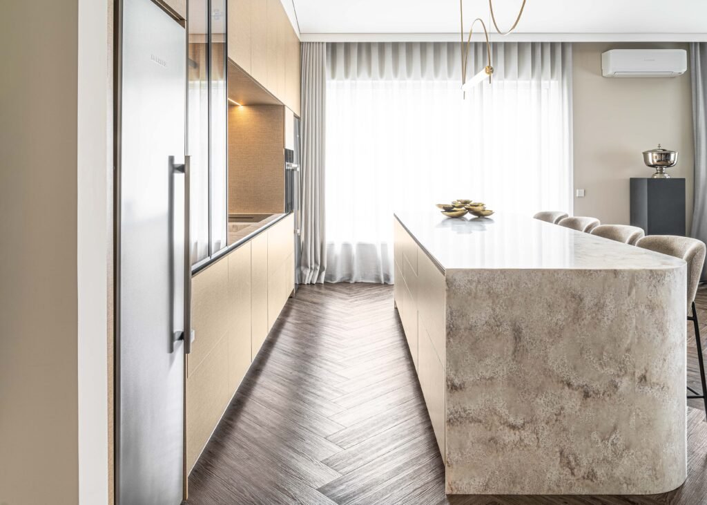 Side view of a modern kitchen with integrated fridge, light cabinetry and a textured stone island – AK Interior Design, Cork