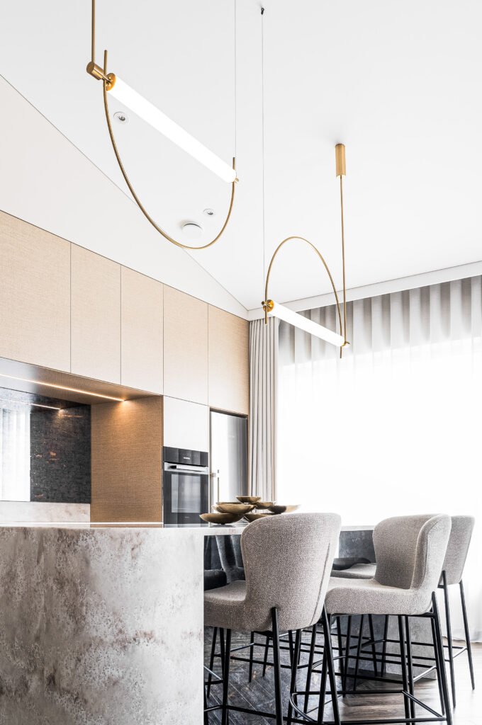 Wide view of a modern kitchen with stone island, soft bar stools and curved gold pendant lights – AK Interior Design, Cork