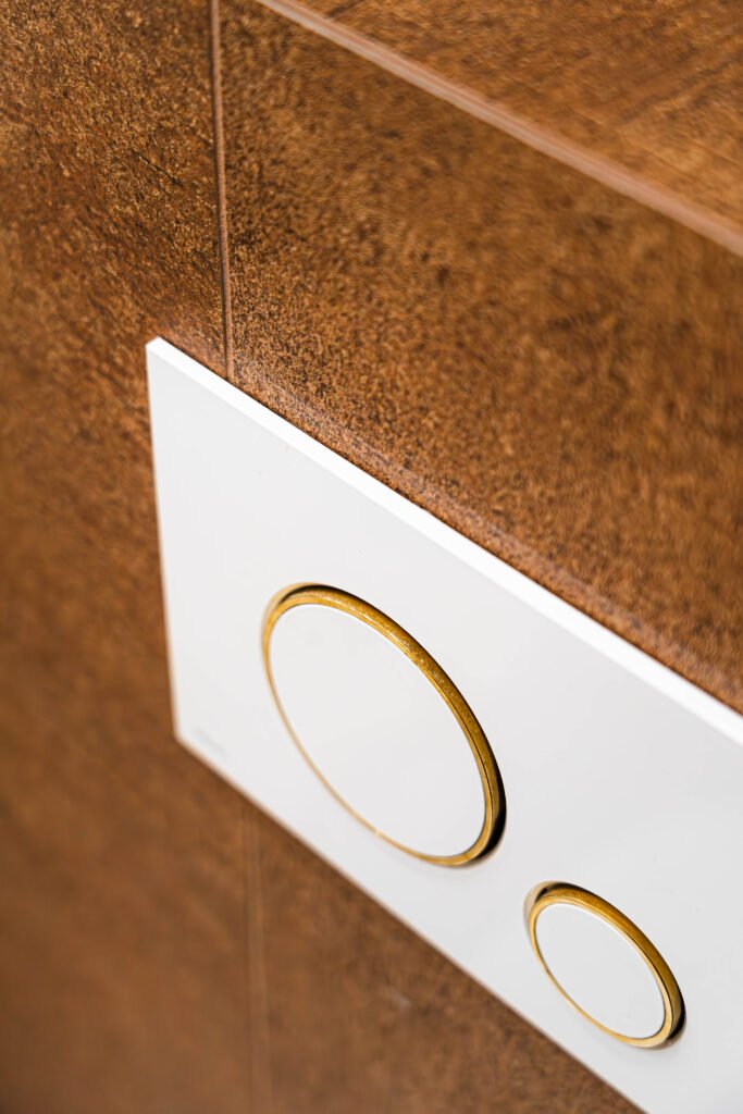 White flush plate with brass rings on textured brown bathroom wall, AK Interior Design, Cork, Ireland.