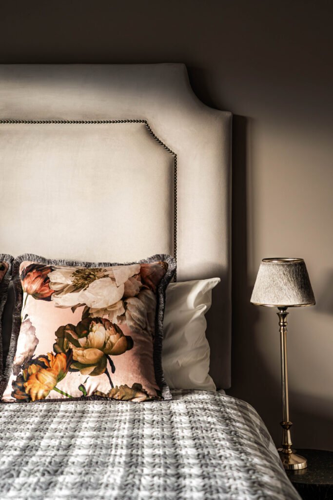 Close-up of upholstered headboard, floral pillows and classic bedside lamp – Monkstown Full House Design by AK Interior.