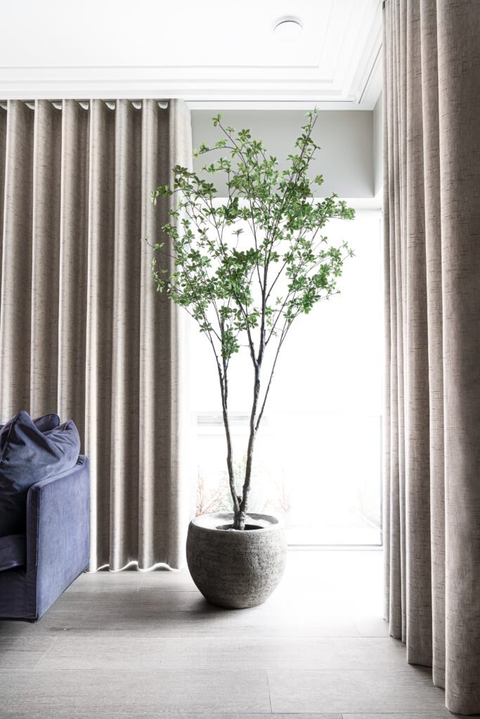 Living room with blue sofa, tall indoor plant and dual-layer curtains – West Cork Waterfront, residential project by AK Interior, Cork, Ireland.
