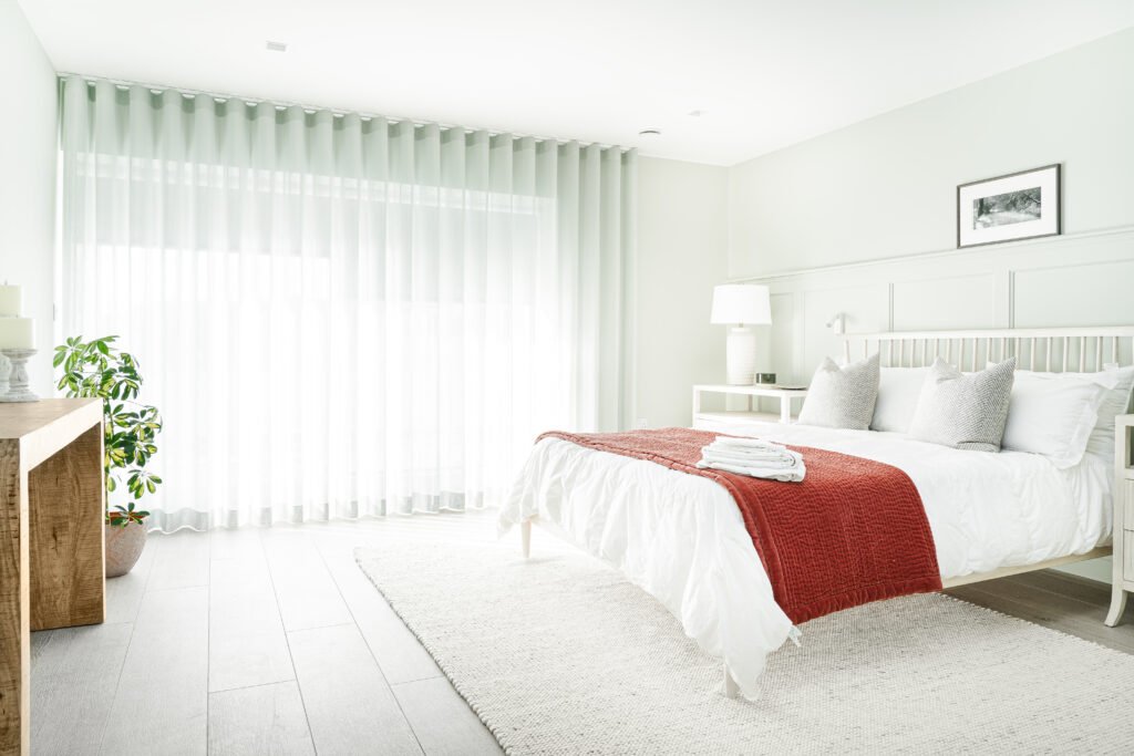 Bright bedroom with large window, white bedding and red accent throw – West Cork Waterfront, residential project by AK Interior, Cork, Ireland.