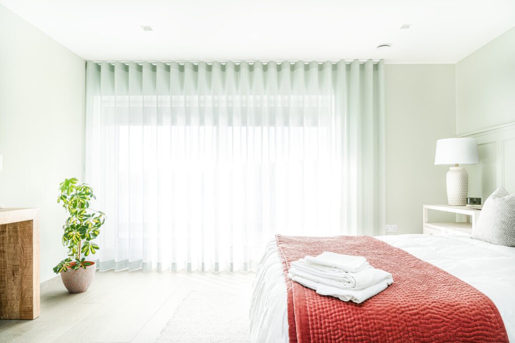 Bedroom with sheer white curtains and bed styled with red throw blanket – West Cork Waterfront, residential project by AK Interior, Cork, Ireland.