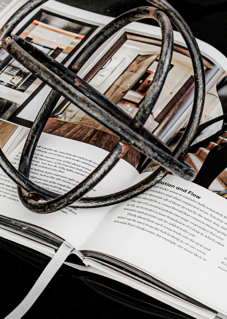 Close-up of metal armillary sculpture resting on open design book. Rosscarbery Residence residential project, AK Interior.