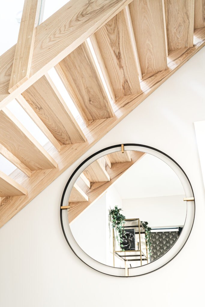 Light oak staircase with sculptural round mirror reflecting shelves. Rosscarbery Residence residential project, AK Interior.