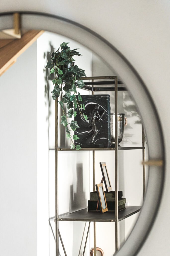 Brass and glass shelving unit seen through large round mirror. Rosscarbery Residence residential project, AK Interior.