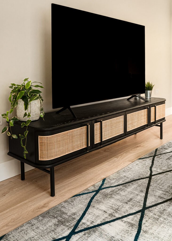 Media wall with black TV unit, woven fronts and potted greenery. Rosscarbery Residence residential project, AK Interior.