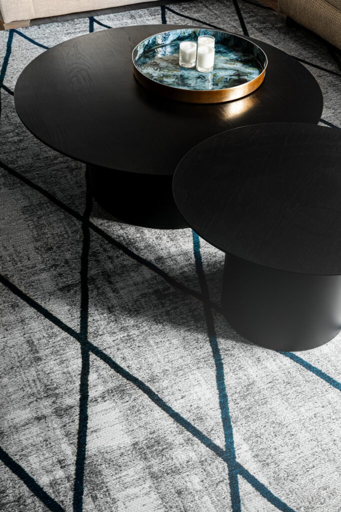 Pair of round black coffee tables on grey rug with blue graphic lines. Rosscarbery Residence residential project, AK Interior.