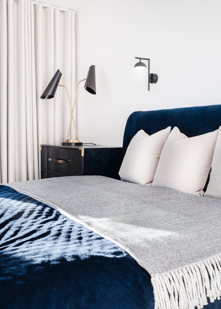 Modern bedroom with navy upholstered bed, neutral bedding and black wall lights. Rosscarbery Residence residential project, AK Interior.
