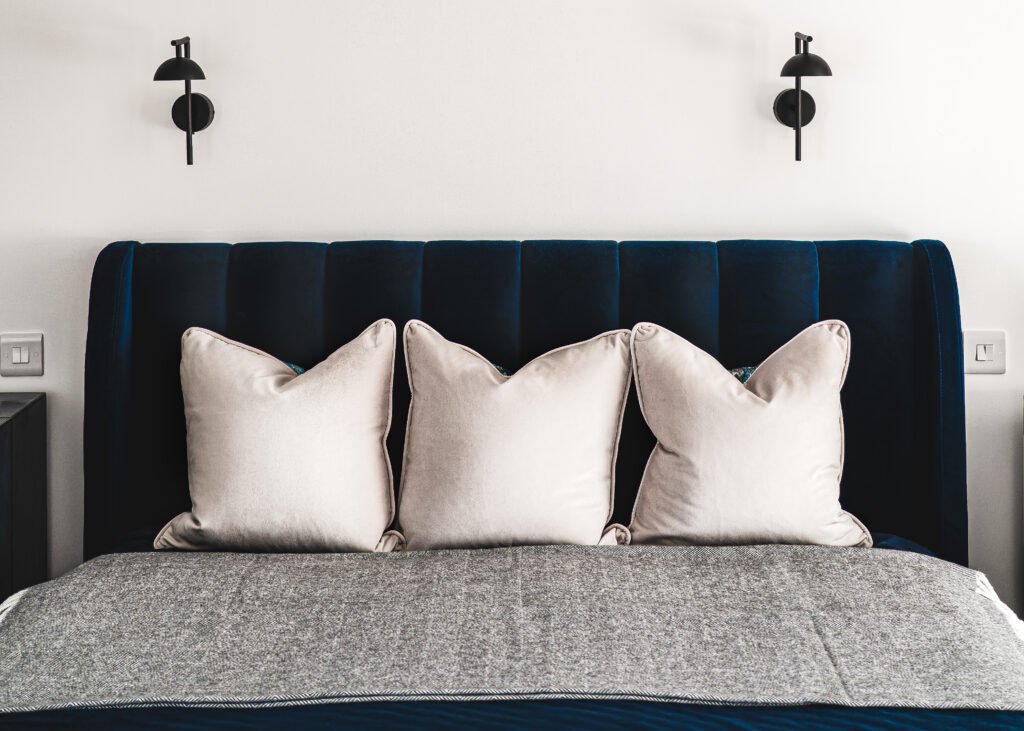 Front view of navy velvet headboard with three cream cushions and grey throw. Rosscarbery Residence residential project, AK Interior.