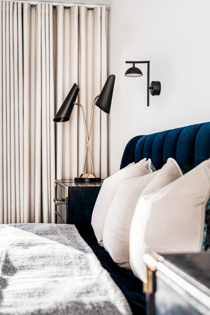 Side view of bedroom with full-height curtains, black sconces and navy bed. Rosscarbery Residence residential project, AK Interior.